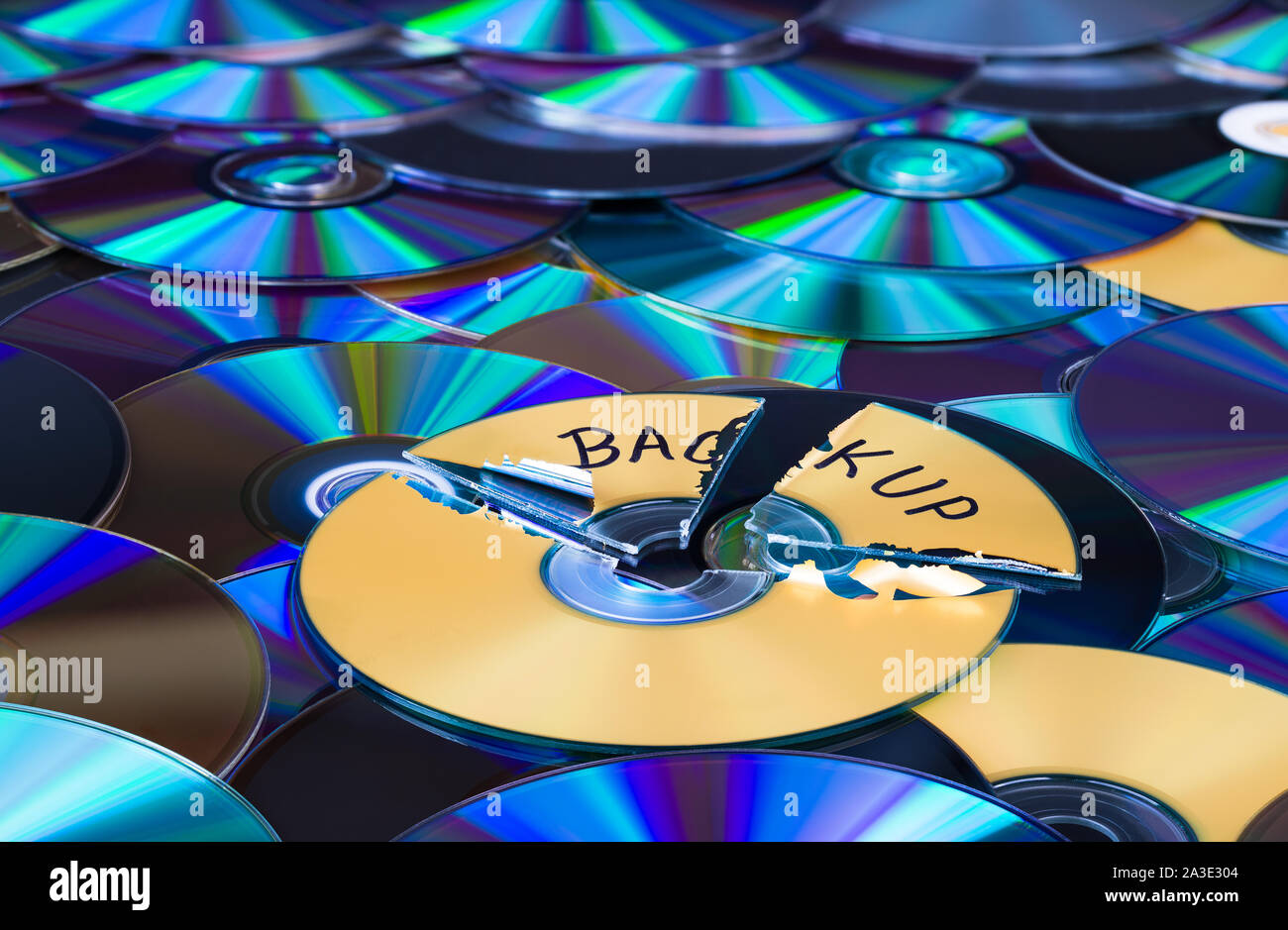 Damaged compact disc. Secure backup and disposal of digital personal data. Broken optical storage device on green-blue texture. Old archiving media. Stock Photo