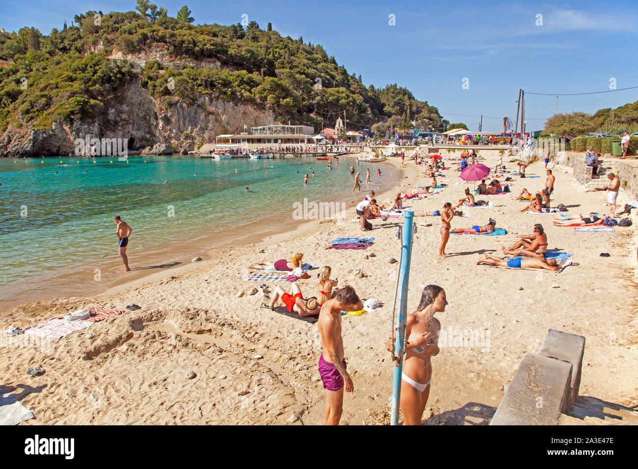 Holidaymakers and tourists enjoying the sunshine on the sandy beach at the Greek holiday resort of Paleokastrita on the Island of Corfu Greece Stock Photo