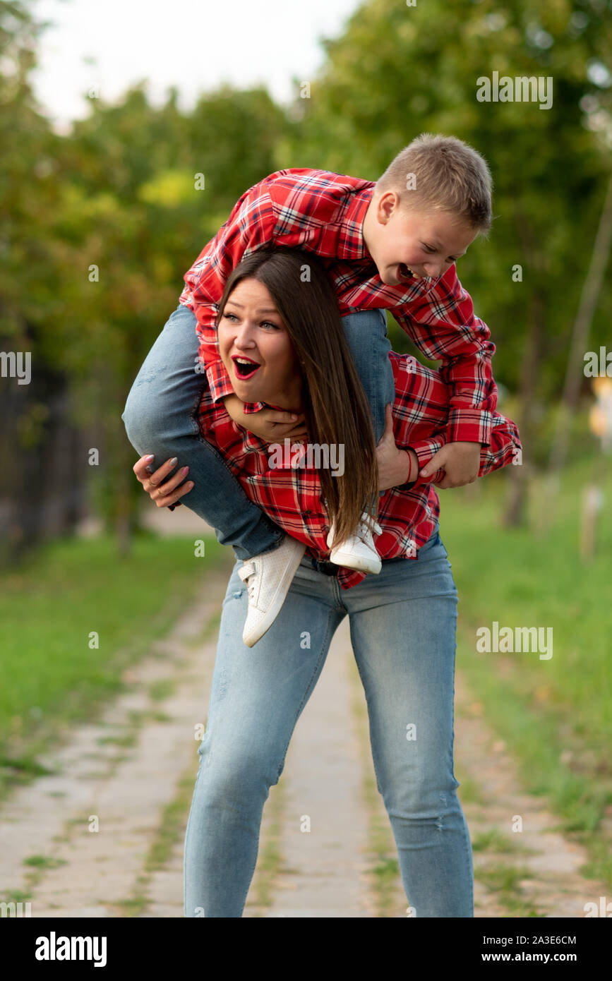 Mom, with a surprised expression on her face, holds a smiling son on her shoulders. Stock Photo