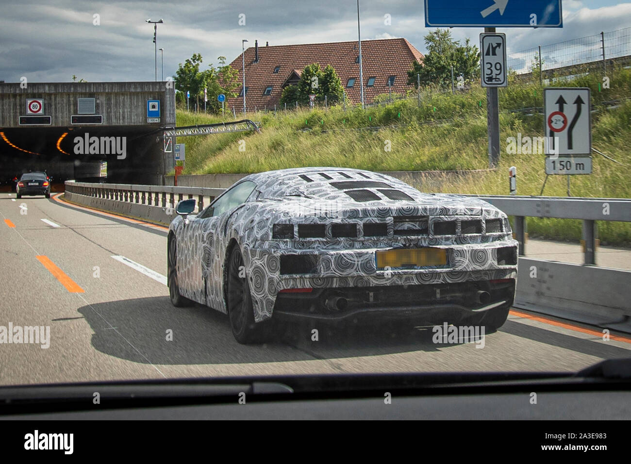 A McLaren GT prototype test vehiche photographed doing road tests in Switzerland. Rear end and air intake heavily camouflaged with both camo tape and extra panels. Tail lights are hidden under mesh panel. The new GT model was first announced at the 2019 Geneva Auto Salon, but details about the car was first released in May same year. These images were taken in June 2019 and differs from earlier photos in having extra panels popped onto the rear and the side, as well as tail lights camouflaged. The outline of the tail lights are visible through the tape. Stock Photo