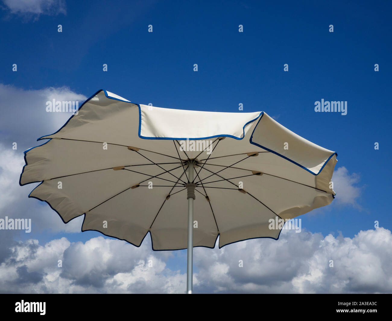 white beach umbrella viewed from above sways moved by the sea breeze . Blue sky with  white clouds background, copy space Stock Photo