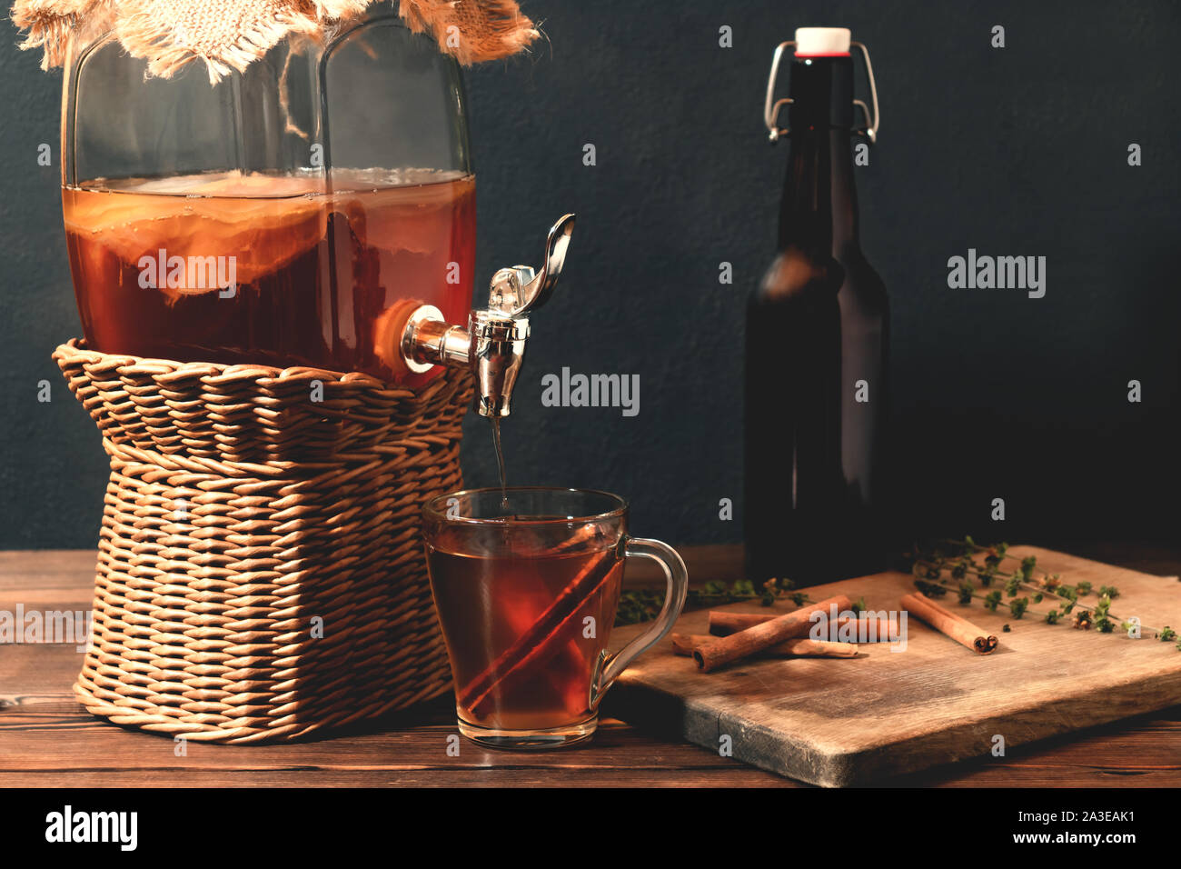 Fresh homemade Kombucha fermented tea drink in jar with faucet and in cup and bottle on black background. Stock Photo