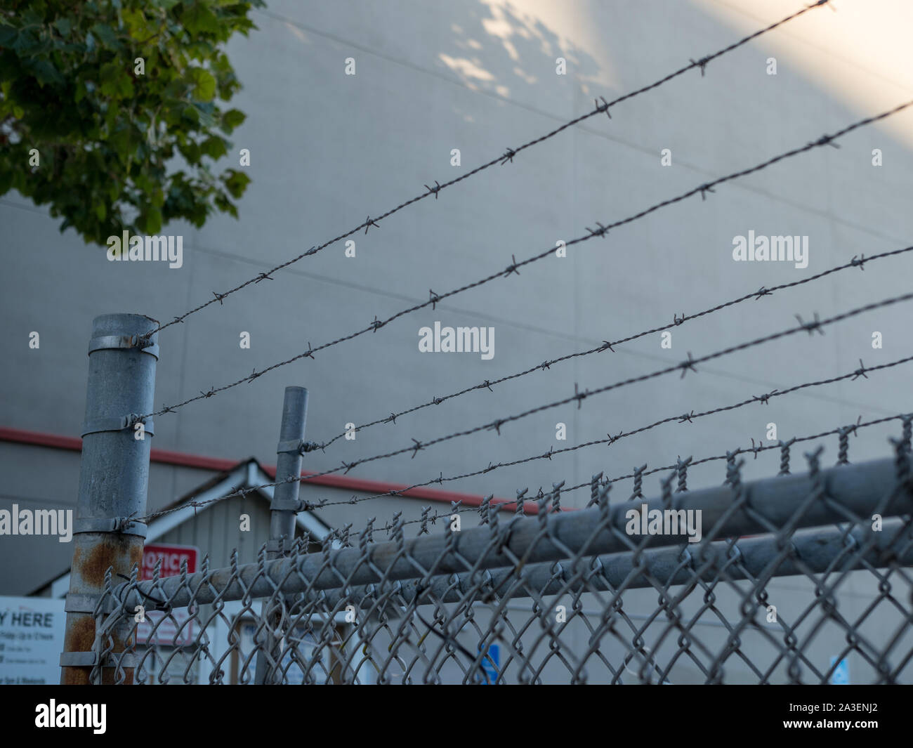 Barbed wire on steel chain link fence blowing entry to warehouse Stock Photo