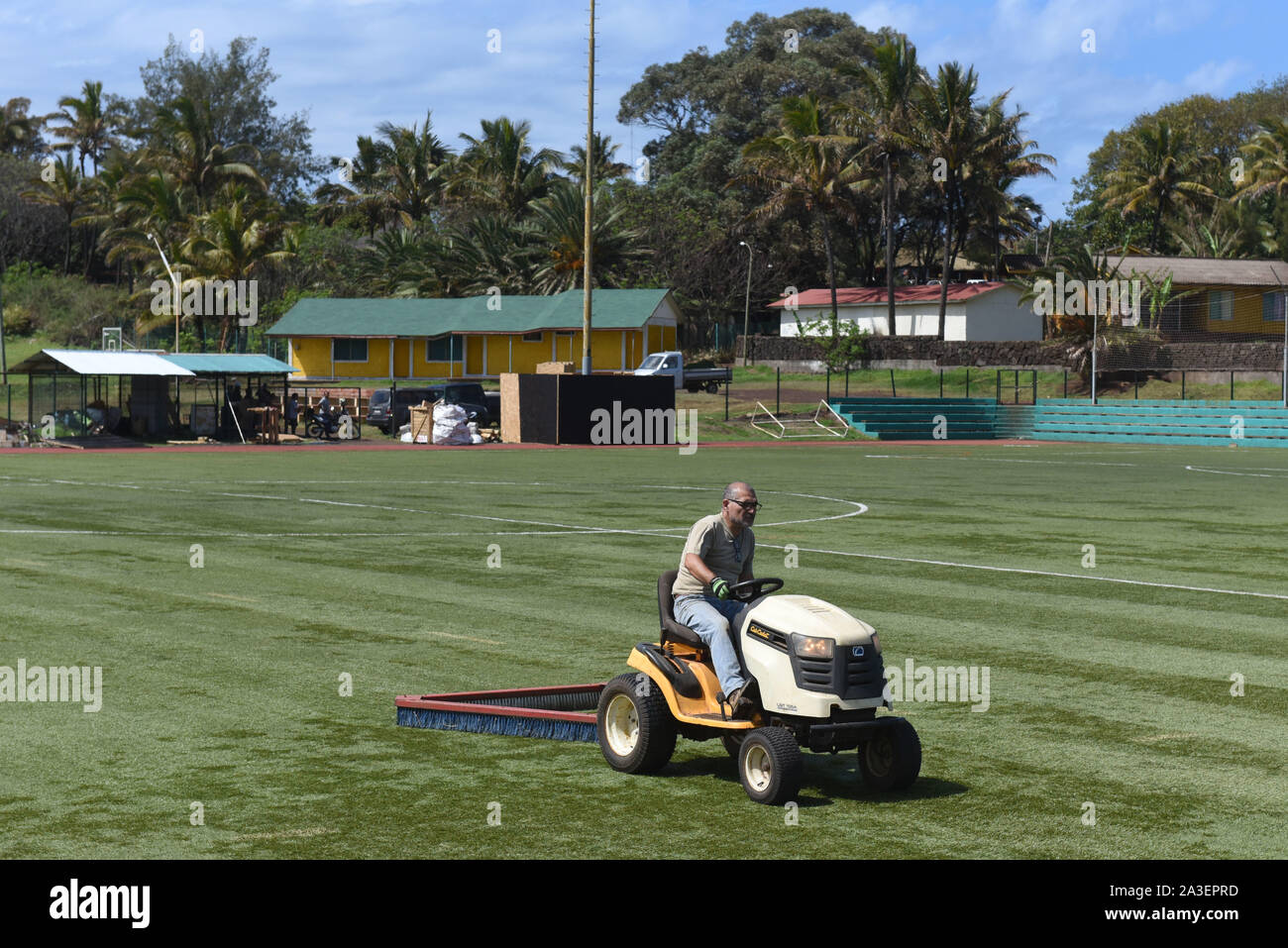 A groundsman cuts the grass with a mower ride on a sports field.Hanga Roa is the capital of Easter Island, a Chilean island in the southeastern Pacific Ocean. The village has around 5,000 inhabitants, which comprises between 87 and 90 percent of the total population of the island. Excluding a small percentage still engaged in traditional fishing and small-scale farming, the majority of the population is engaged in tourism which is the main source of income. Stock Photo