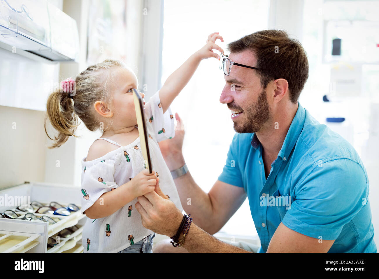 Health care, eyesight and vision concept. Little girl choosing glasses with father at optics store Stock Photo