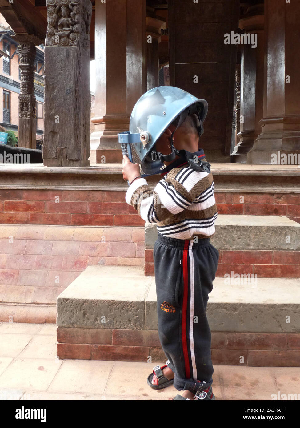 Jeune enfant népalais avec un casque sur la tête devant un temple. Stock Photo