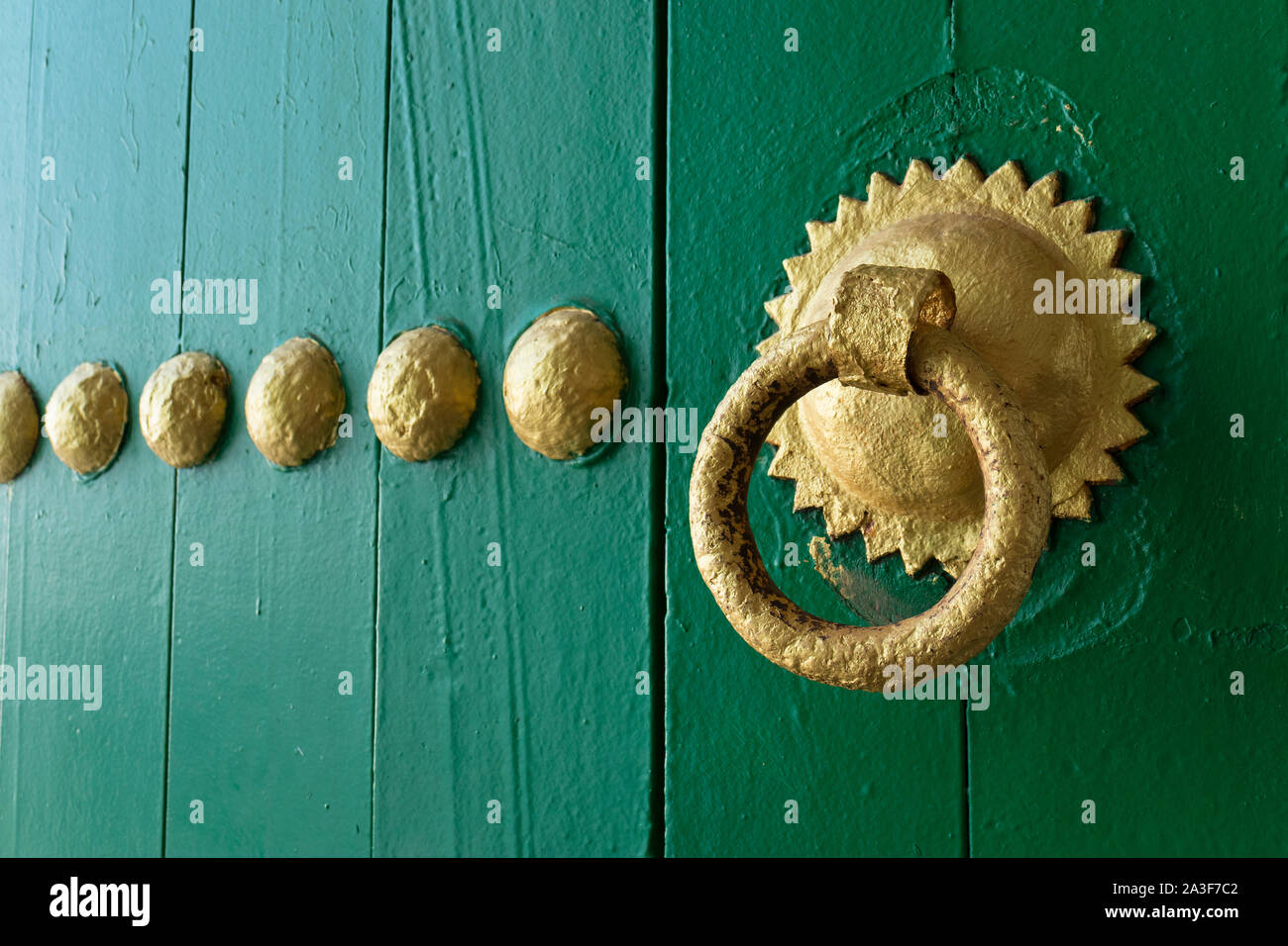 Gold painted doorknocker on a green wooden door in Asilah, Morocco Stock Photo