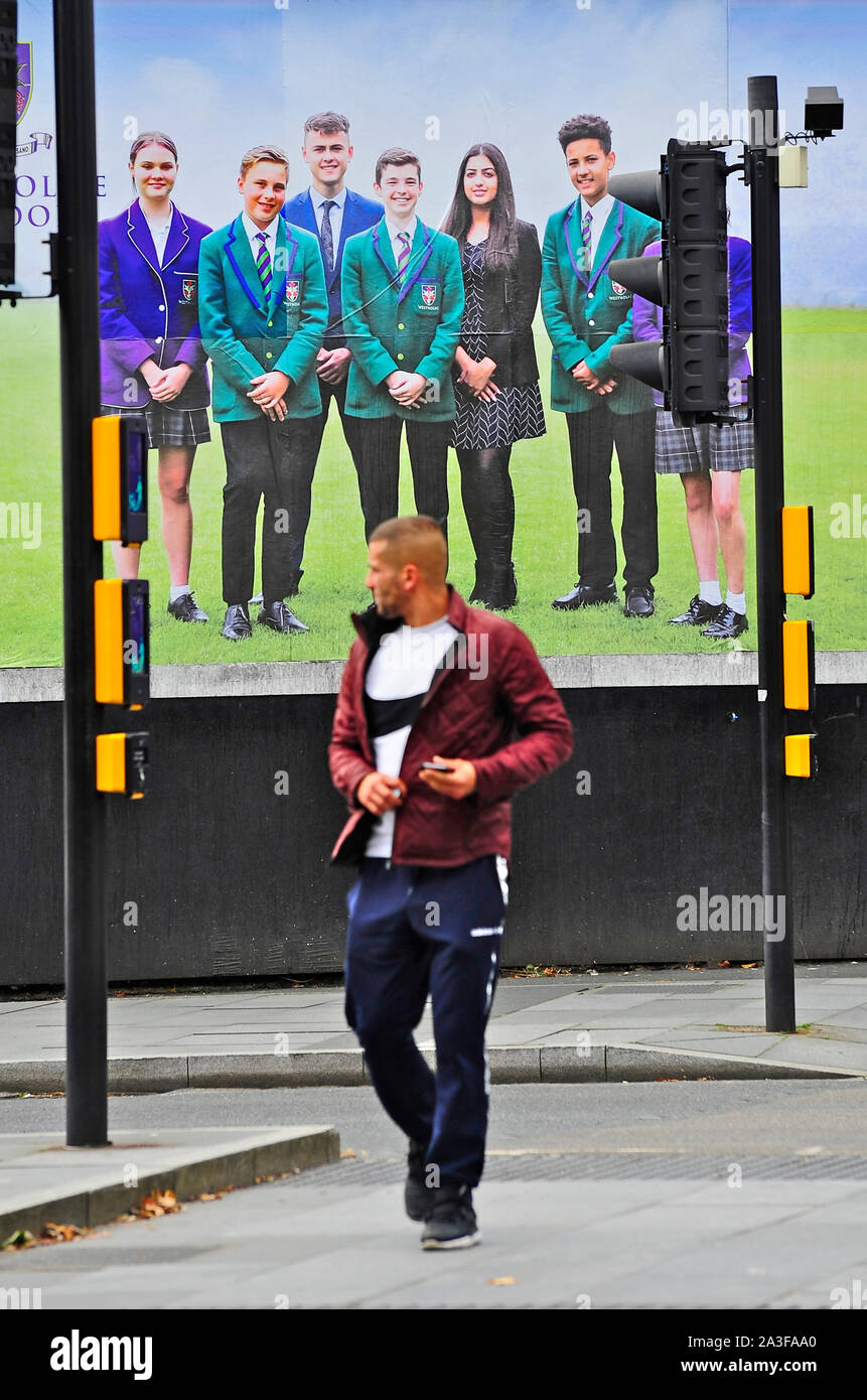 Man crossing signal controlled road junction in front of poster showing smiling children advertising private school Stock Photo