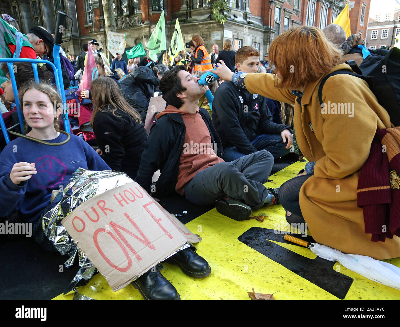 A protester, who has glued himself to the ground at Millbank near to the junction with Great College Street, receives refreshment during an Extinction Rebellion (XR) protest in Westminster, London. Stock Photo