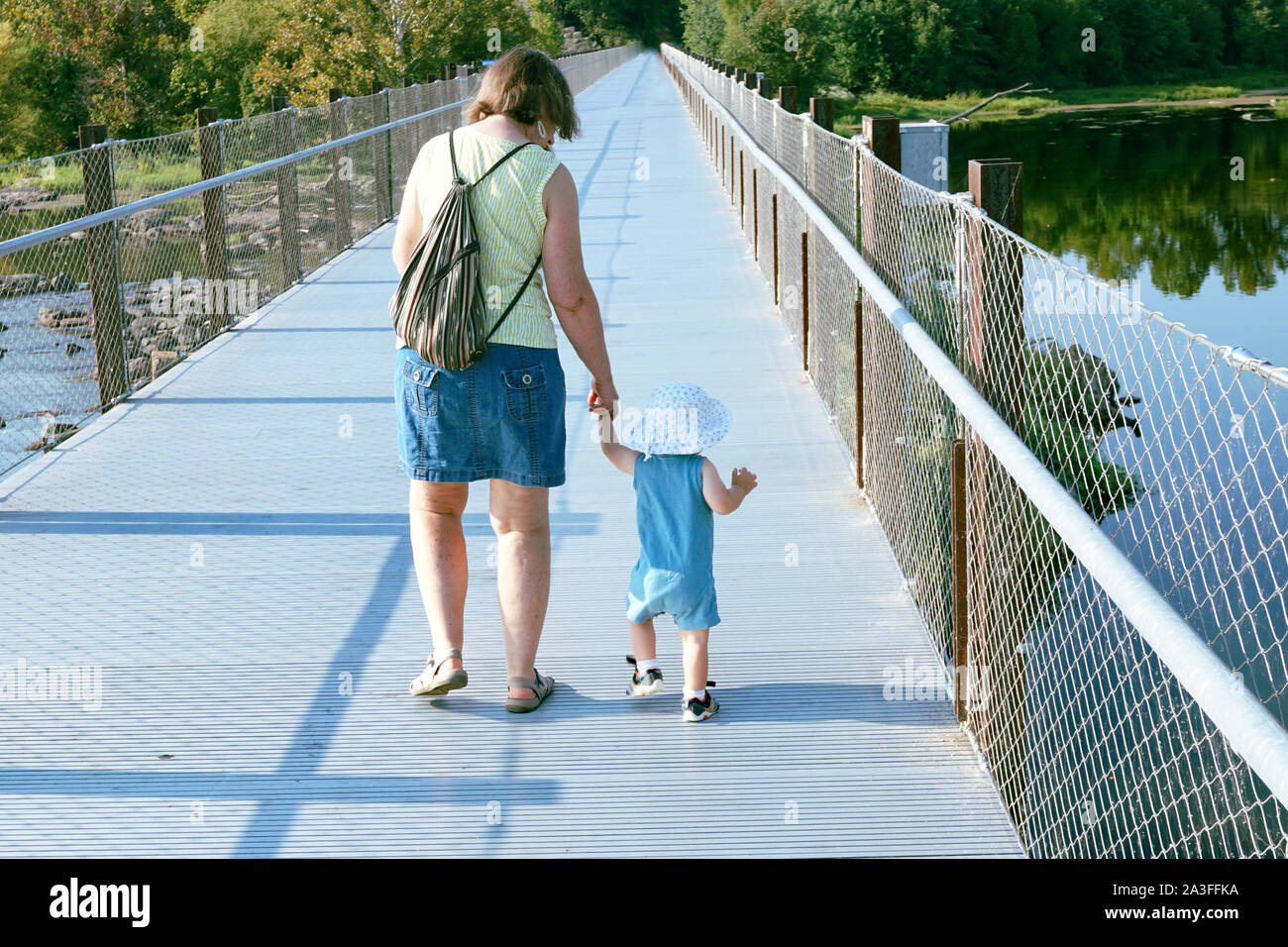 Toddler holding hands and walking with grandmother on a bridge over a river Stock Photo