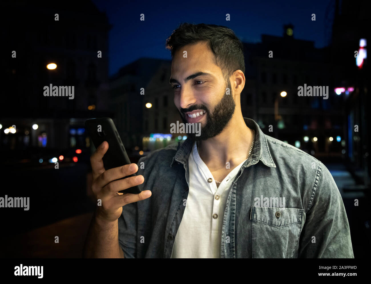Young bearded smiling arab man holding smartphone outdoors night street Stock Photo