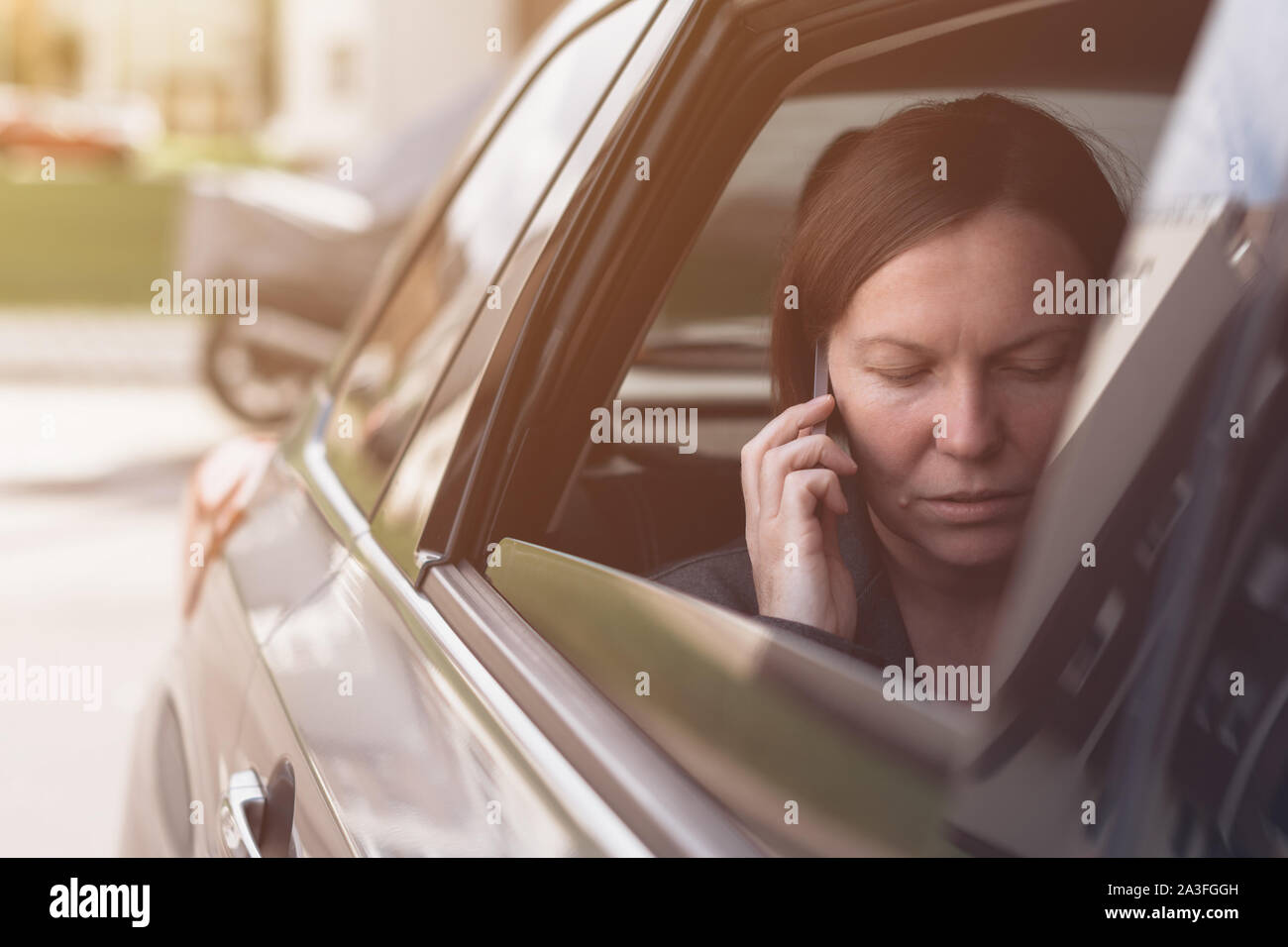 Businesswoman talking on mobile phone inside of company car while sitting at the back seat Stock Photo