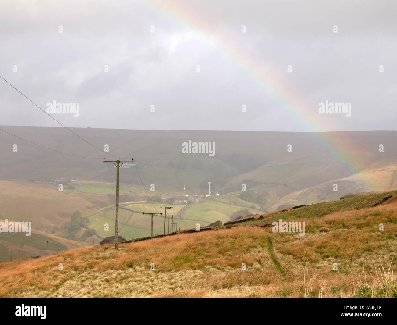 High on the bleak dreary exposed pennines with wind rain low clouds and a rainbow with power lines above Marsden Huddersfield Yorkshire England Stock Photo