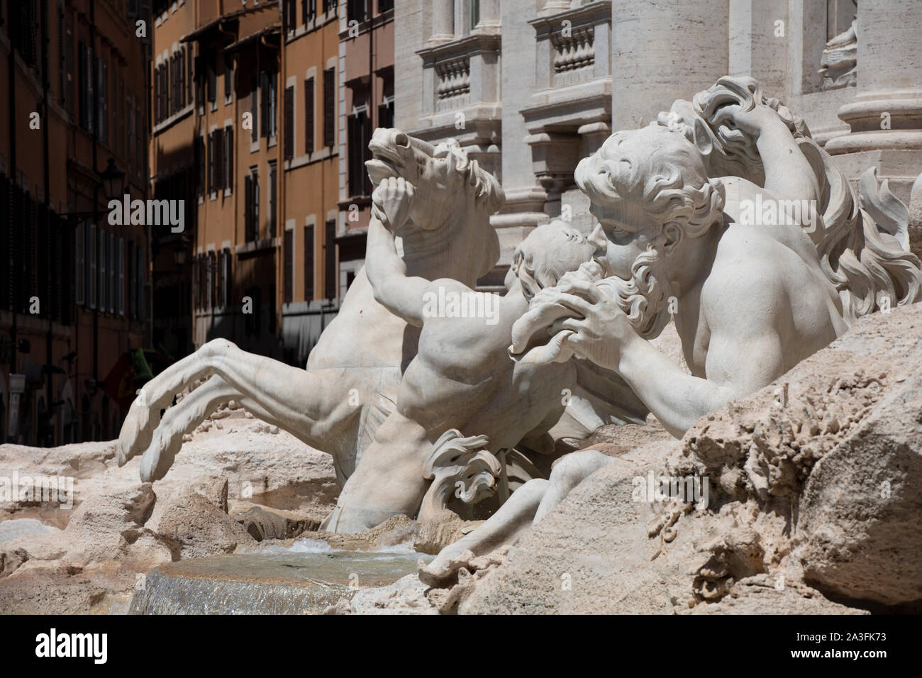 Statues on the Trevi Fountain in Rome, showing the tritons and sea horses struggling on the rocks. In the background are some traditional roman houses Stock Photo