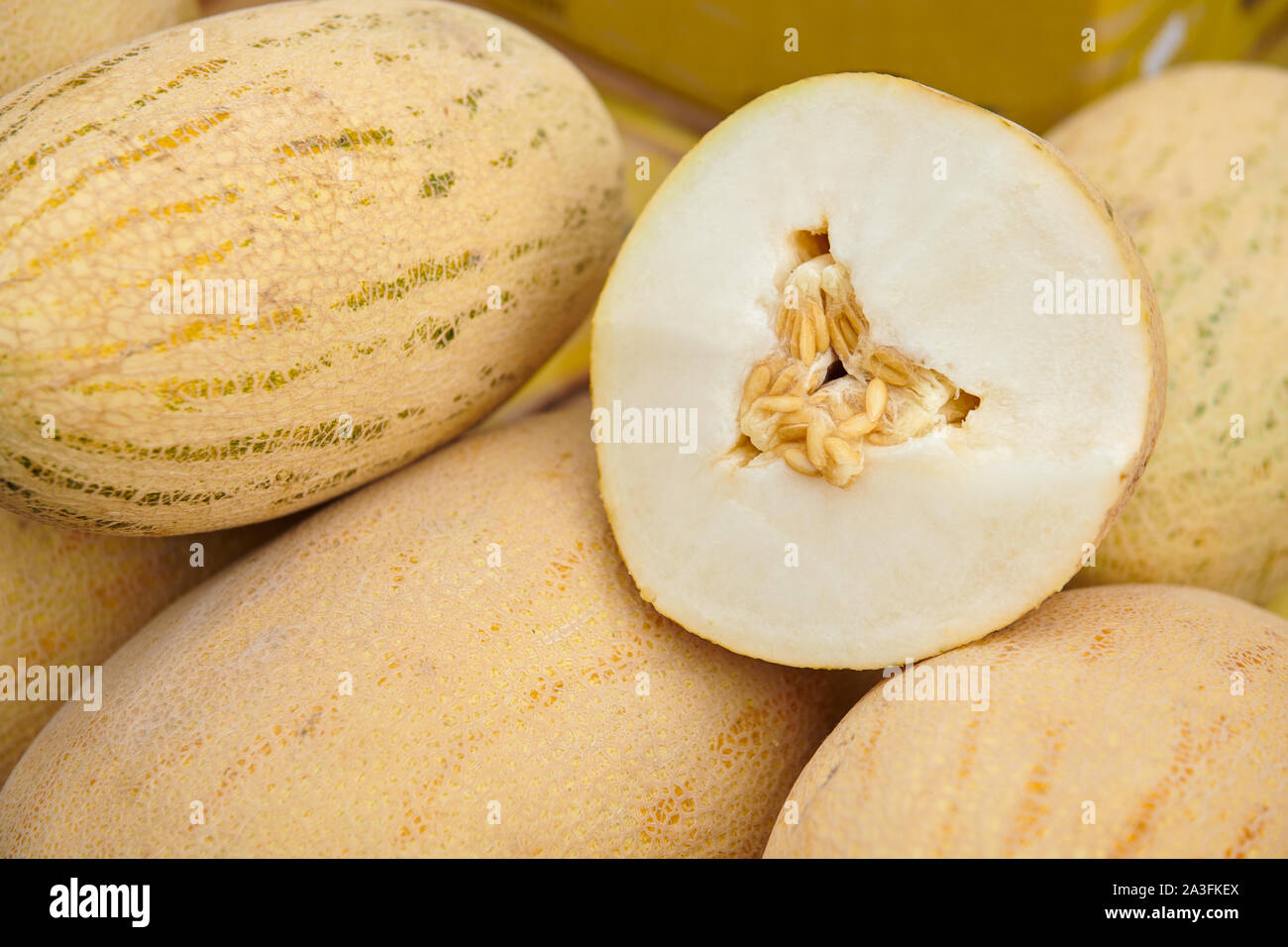 Ripe melon cut in half laying on a bunch of yellow melons. Melon with seeds. Degustation at the market. Stock Photo