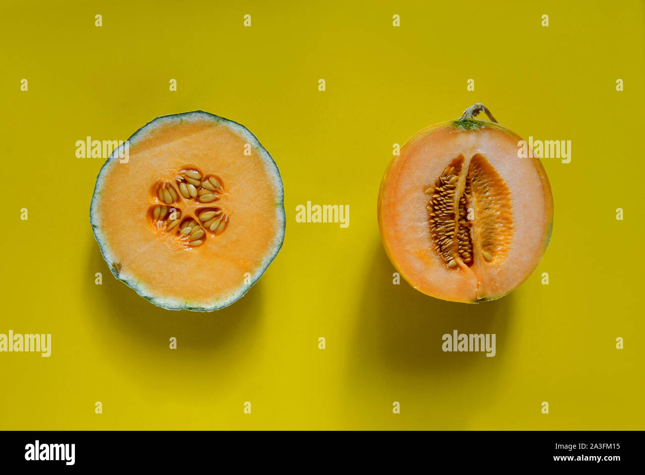 Cantaloupe sliced in half with whole cantaloupe isolated on yellow background Stock Photo