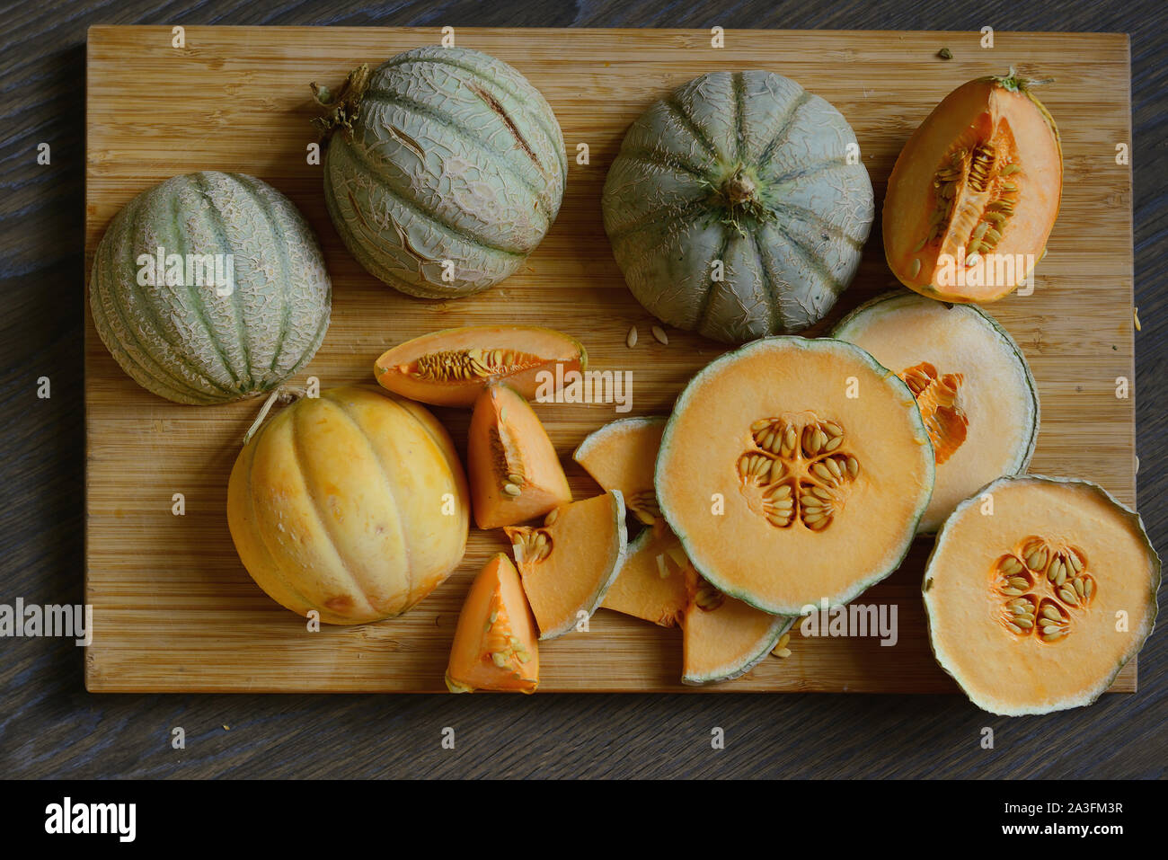Heads of cantaloupe and pieces of melon of different shapes on the wooden surface.Rustic style.Flat lay. Stock Photo