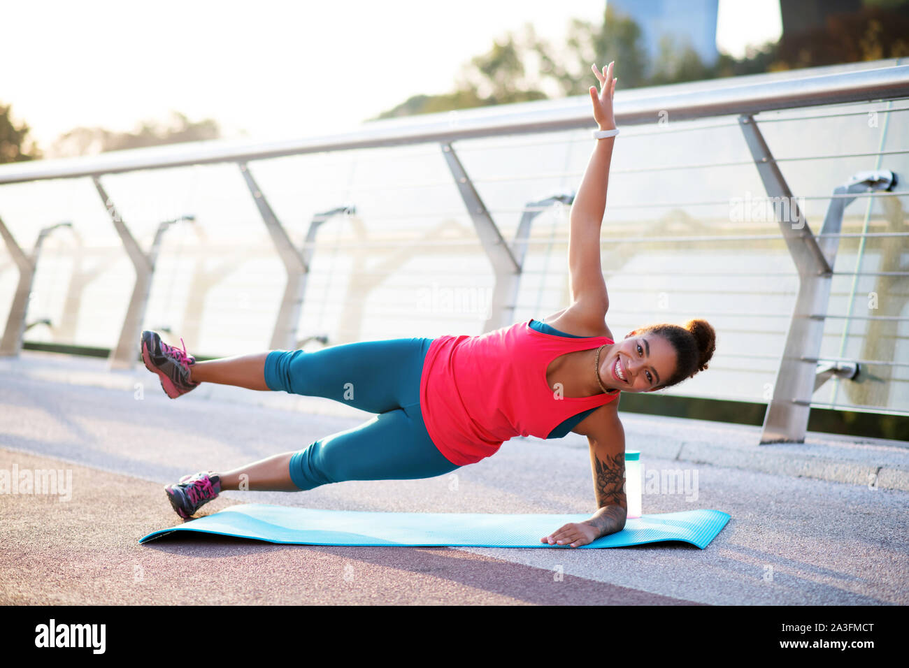 Young beautiful plus size woman in sporty top and leggings with red  headphones sitting on knees on yoga mat while thoughtfully looking aside in  city park Stock Photo