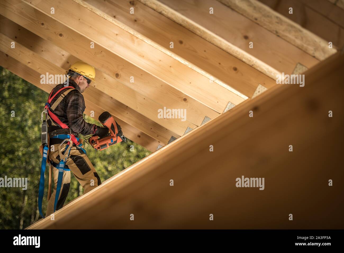 Professional Carpenter Contractor Job. Caucasian Worker with Nail Gun and the Wooden House Roof Frame. Industrial Theme. Stock Photo