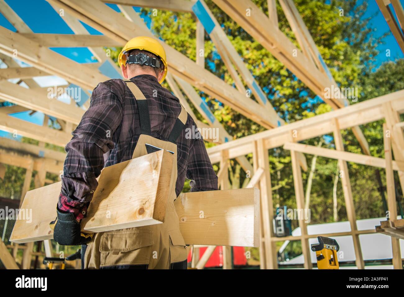 Caucasian Construction Worker Moving Wood Elements. Wooden Building Frame in the Background. Industrial Theme. Stock Photo