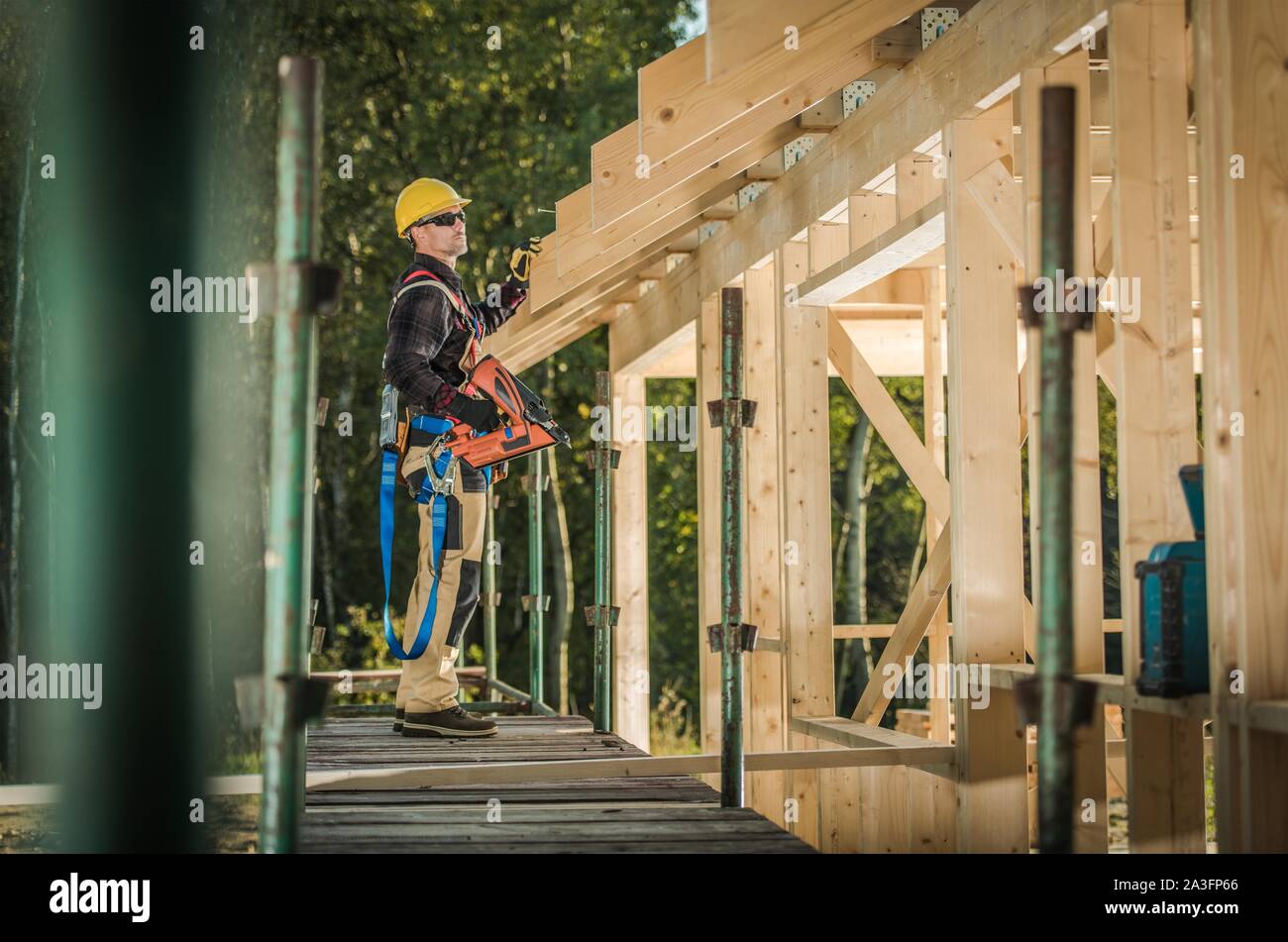 Caucasian Construction Contractor in His 30s with Nail Gun. Wood House Frame Building. Industrial Theme. Stock Photo