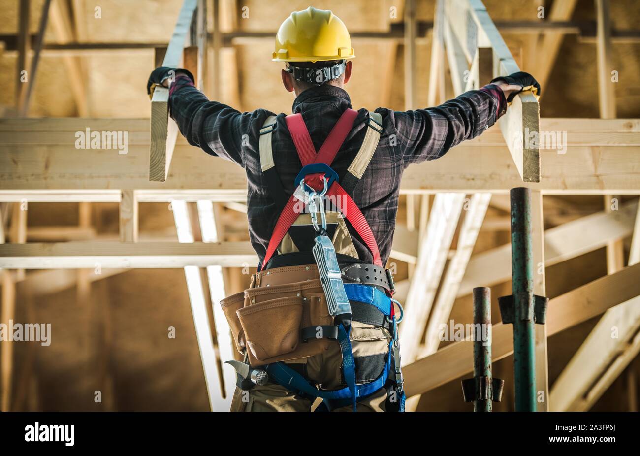 Wood House Construction Challange. Caucasian Carpenter Contractor Wearing Safety Harness in Front of New Developed wood Frame Home. Construction Indus Stock Photo