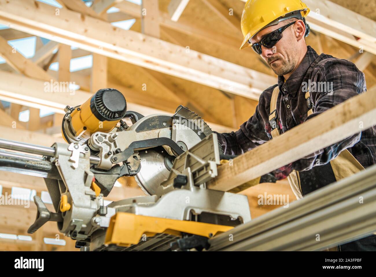 Powerful Wood Construction Electric Saw. Caucasian Carpenter in His 30s Cutting Wooden Elements. Industrial Theme. Stock Photo