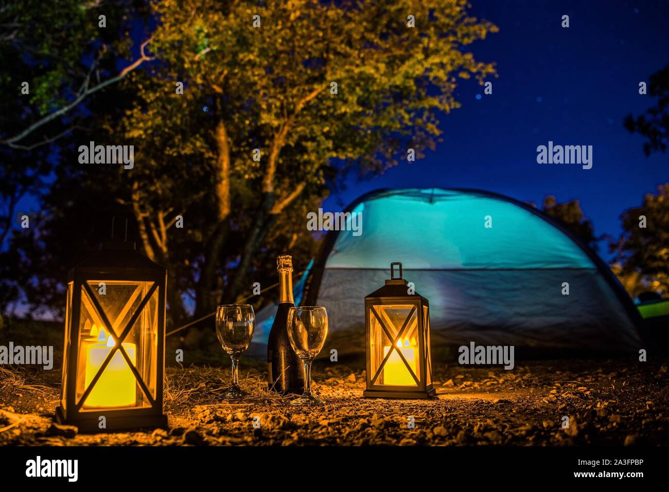 Romantic Camping Night with Bottle of Good Prosecco, Two Glasses, Candle Lanterns and Starry Night. Scenic Getaway with Extras. Stock Photo