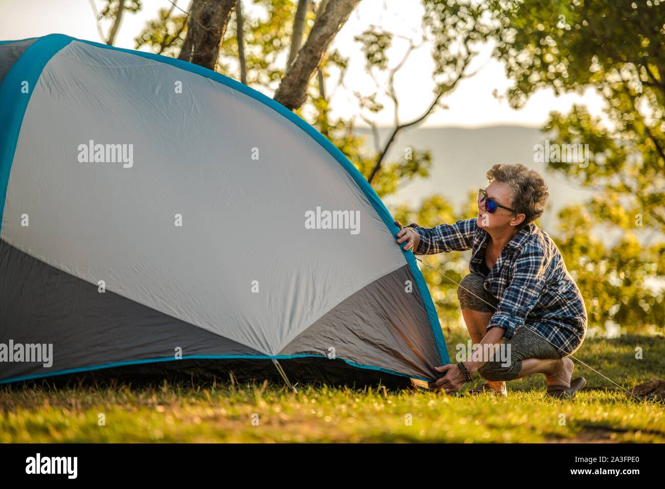 Summer Vacation in a Tent. Retired Caucasian Woman in Her 60s Preparing Her Tent Checking Material Tension. Stock Photo