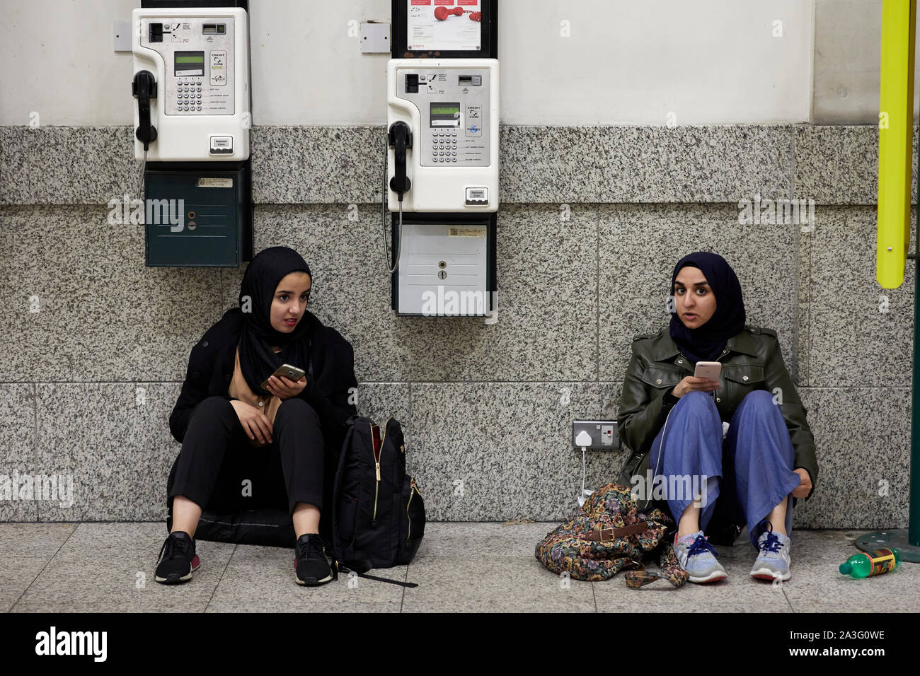 Sound girls using a plug socket to charge their mobile phones before travelling  Central Station Stock Photo