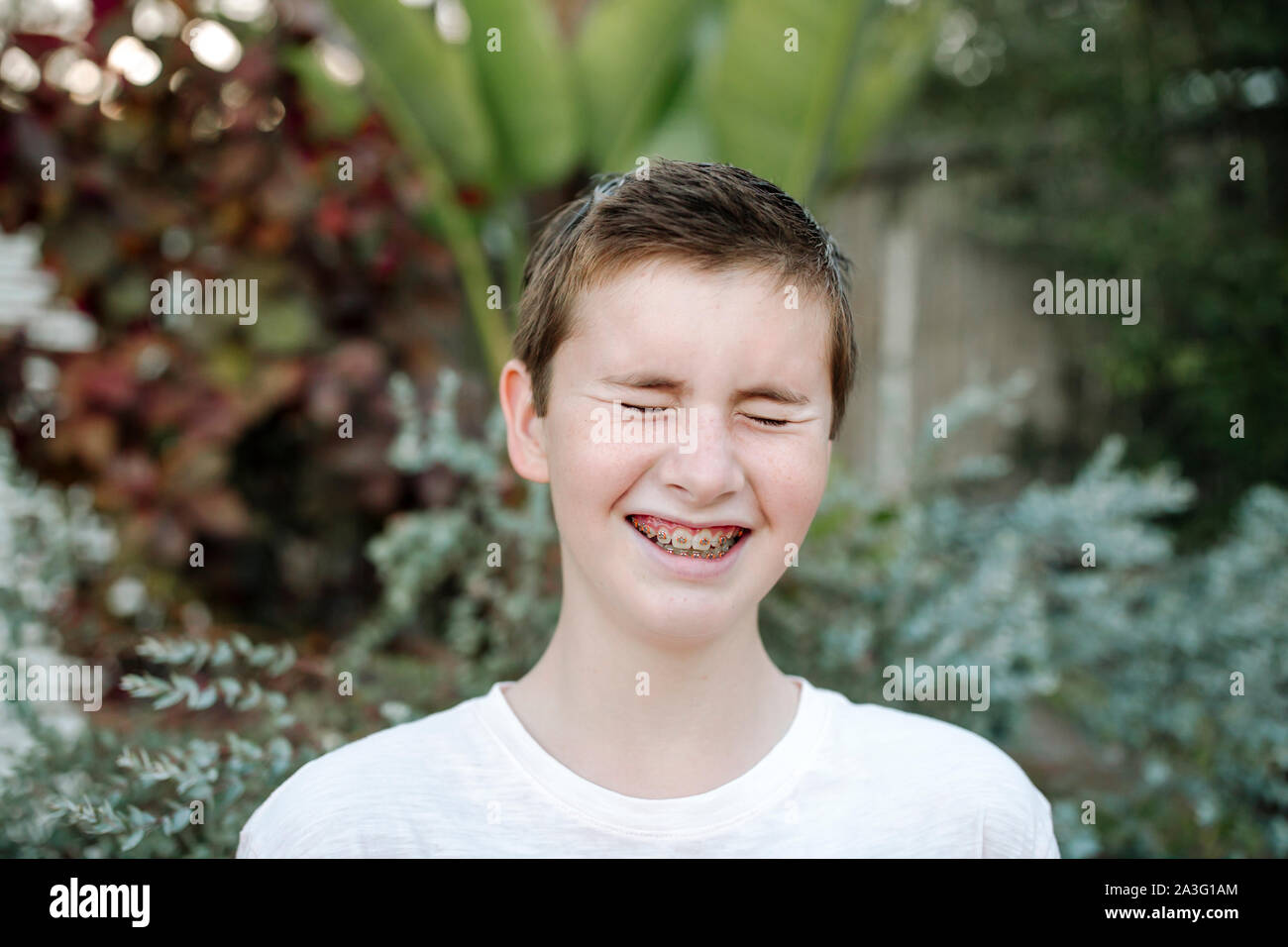 Laughing preteen boy with short hair and braces near lush plants Stock Photo