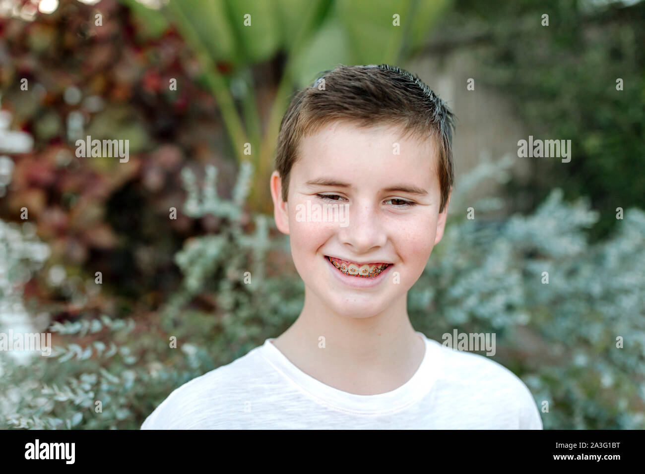 Smiling preteen boy with braces in white tshirt with lush plants Stock Photo