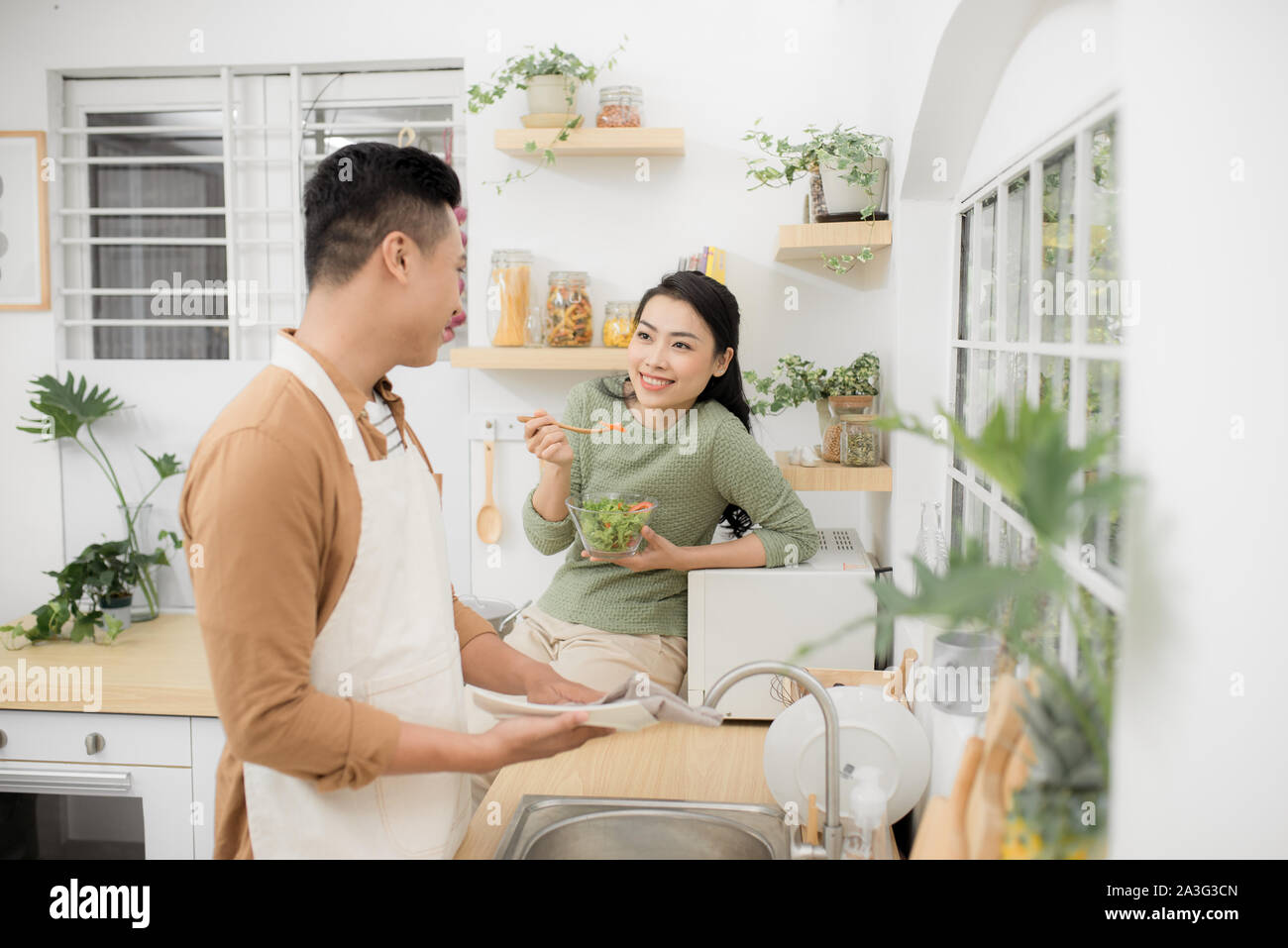 Asian couple eating breakfast early in the morning in the kitchen and having a good time. Stock Photo