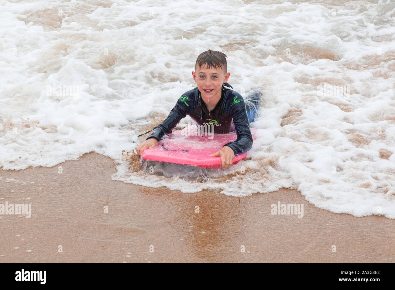 Ten year old boy surfing at Outer Hope Cove, Mouthwell sands beach, Kingsbridge, Devon, England, United Kingdom. Stock Photo