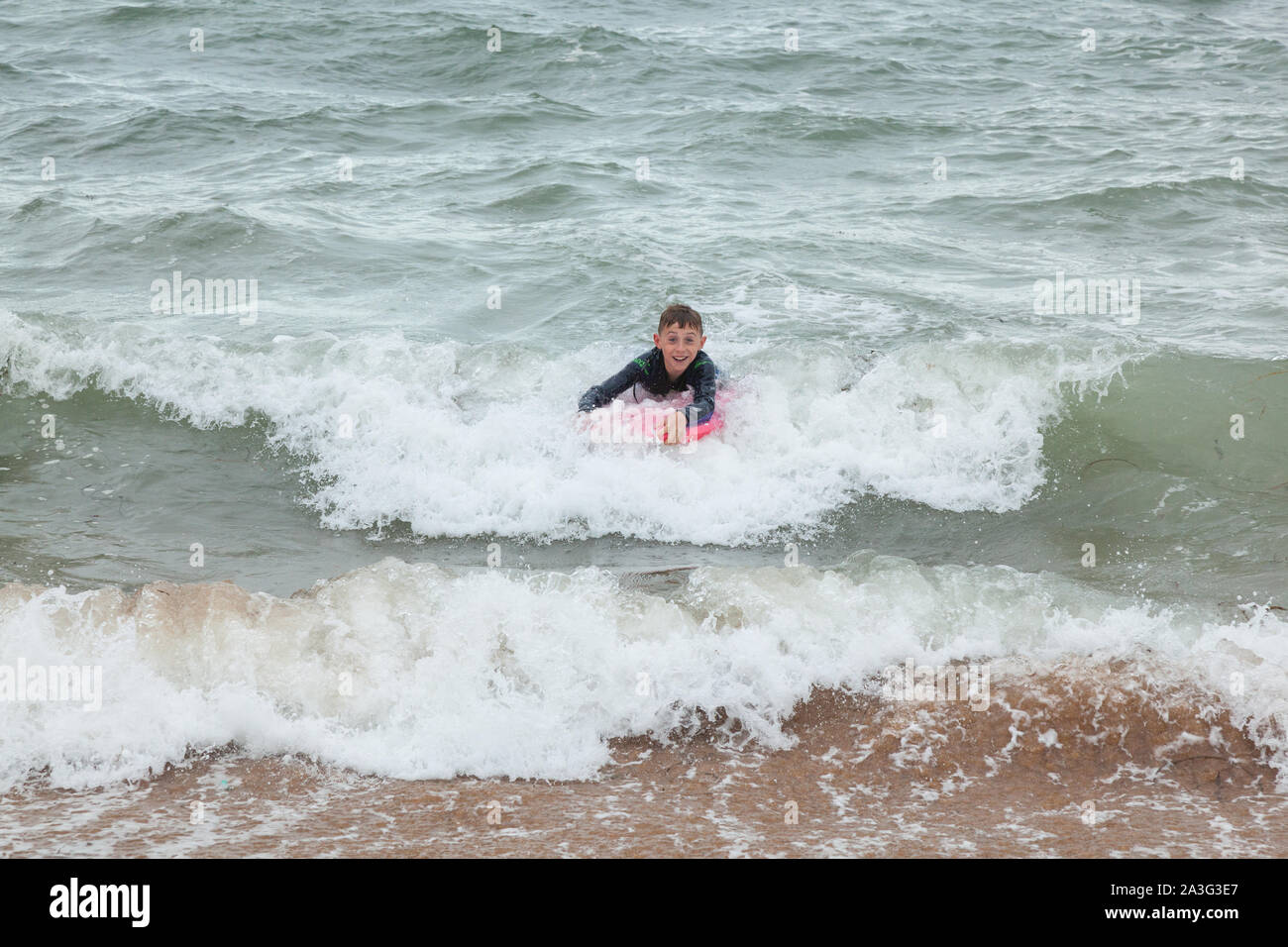 Ten year old boy surfing at Outer Hope Cove, Mouthwell sands beach, Kingsbridge, Devon, England, United Kingdom. Stock Photo