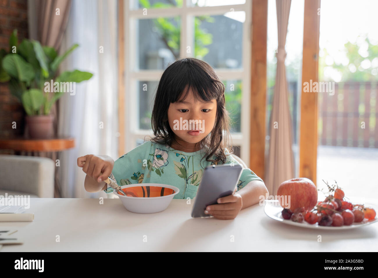 distracted kid using mobile phone while having breakfast on the table Stock Photo