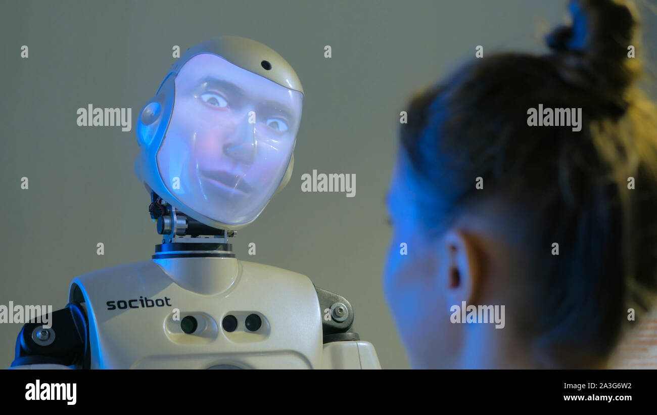 Funny humanoid robot with display face talking with woman Stock Photo