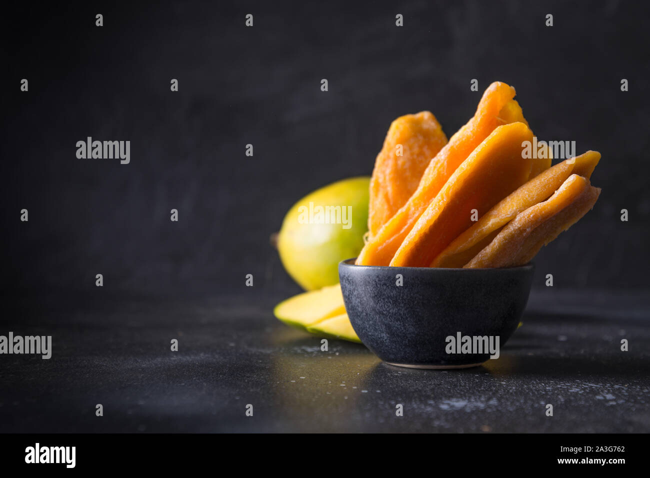 Fresh and dried mango chips on black background. Close up. Space for text. Stock Photo