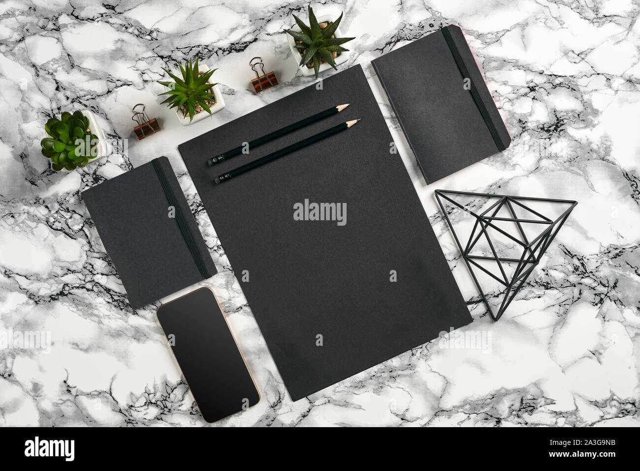 Sheet of black paper, pencils, smartphone, two folders, iron triangle figure, three green plants in the pots and paper clips on marble table with copy Stock Photo