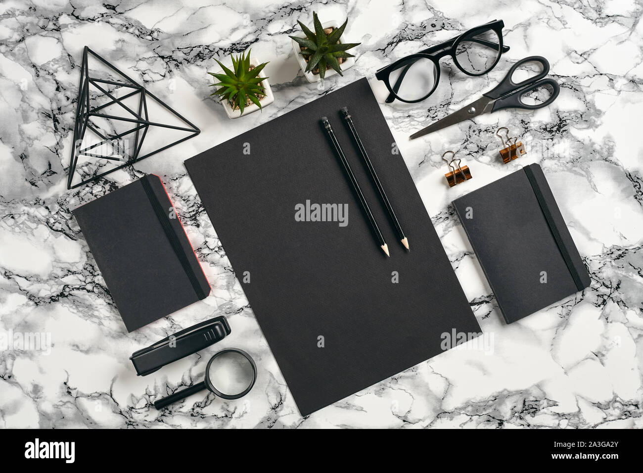 Sheet of black paper, pencils, glasses, magnifier, scissors, stapler, folders, iron triangle figure, green plants in the pots and golden paper clips o Stock Photo