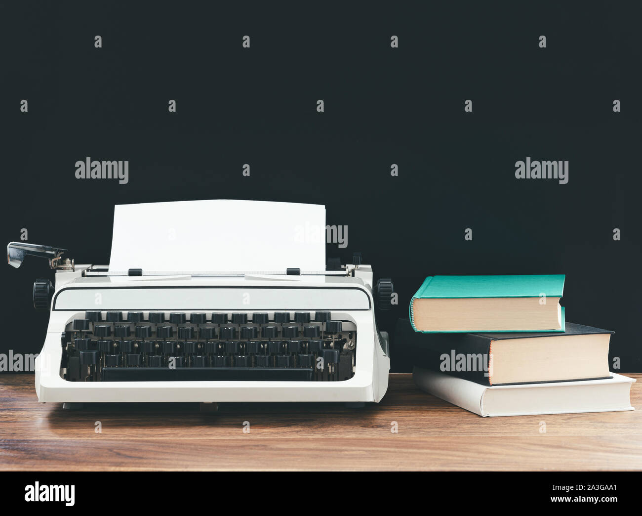 vintage typewriter and stack of books on rustic wooden desk against black background, content creation concept Stock Photo