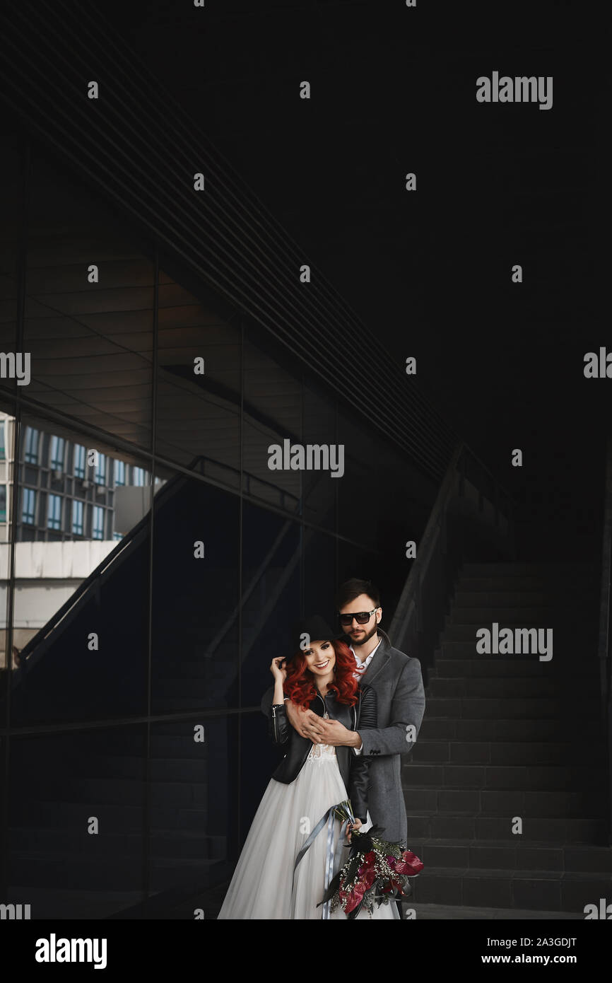 Beautiful couple of lovers hugging outdoors during wedding photoshoot. Slim  young woman with red hair in modish leather jacket and wedding dress and  Stock Photo - Alamy