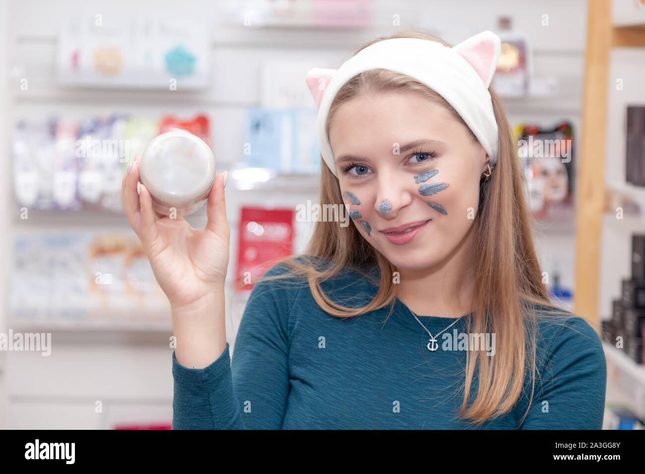 Young cute girl, clay mask in pink headband with ears hold round cream