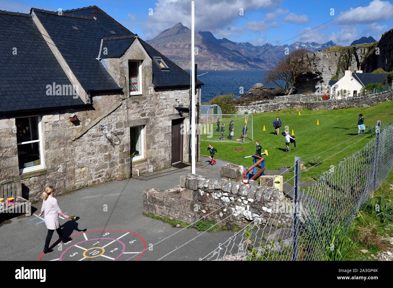 United Kingdom, Scotland, Highlands, Hebrides, Isle of Skye, Elgol village on the shores of Loch Scavaig towards the end of the Strathaird peninsula and the Black Cuillin Mountains in the background, children playing rounders in the school garden Stock Photo