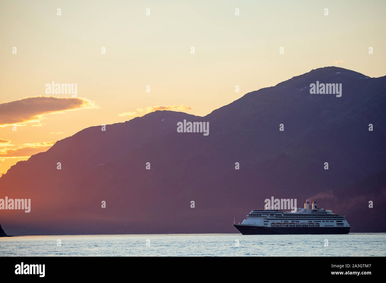 USA, Alaska, Juneau, Setting midnight sun lights cruise ship Holland America Line Amsterdam motoring out of Lynn Canal into Stephens Passage on summer Stock Photo