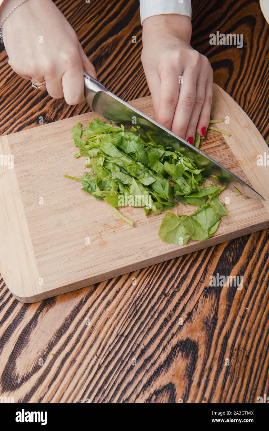 Woman hand cutting spinach using a sharped big kitchen knife on a wooden  cutting table surface with more raw fresh leaves ready to be cut. Kitchen  act Stock Photo - Alamy