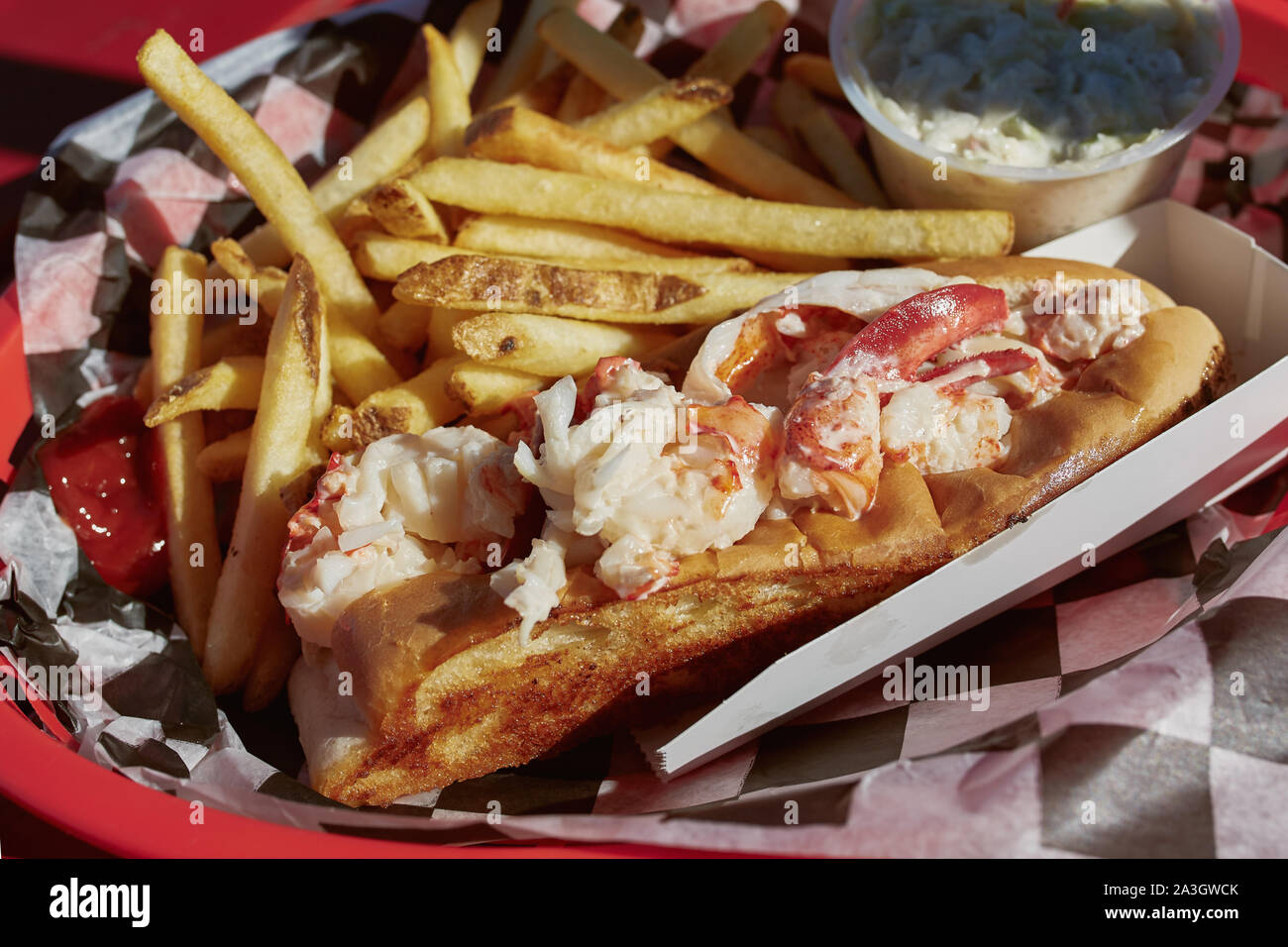 Eating traditional Maine lobster roll with coleslaw and French fries on