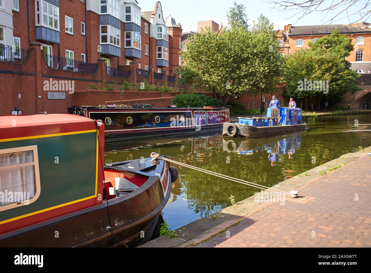 A Canal and River Trust workboat passes moored narrowboat William No102 in the centre of Birmingham Stock Photo