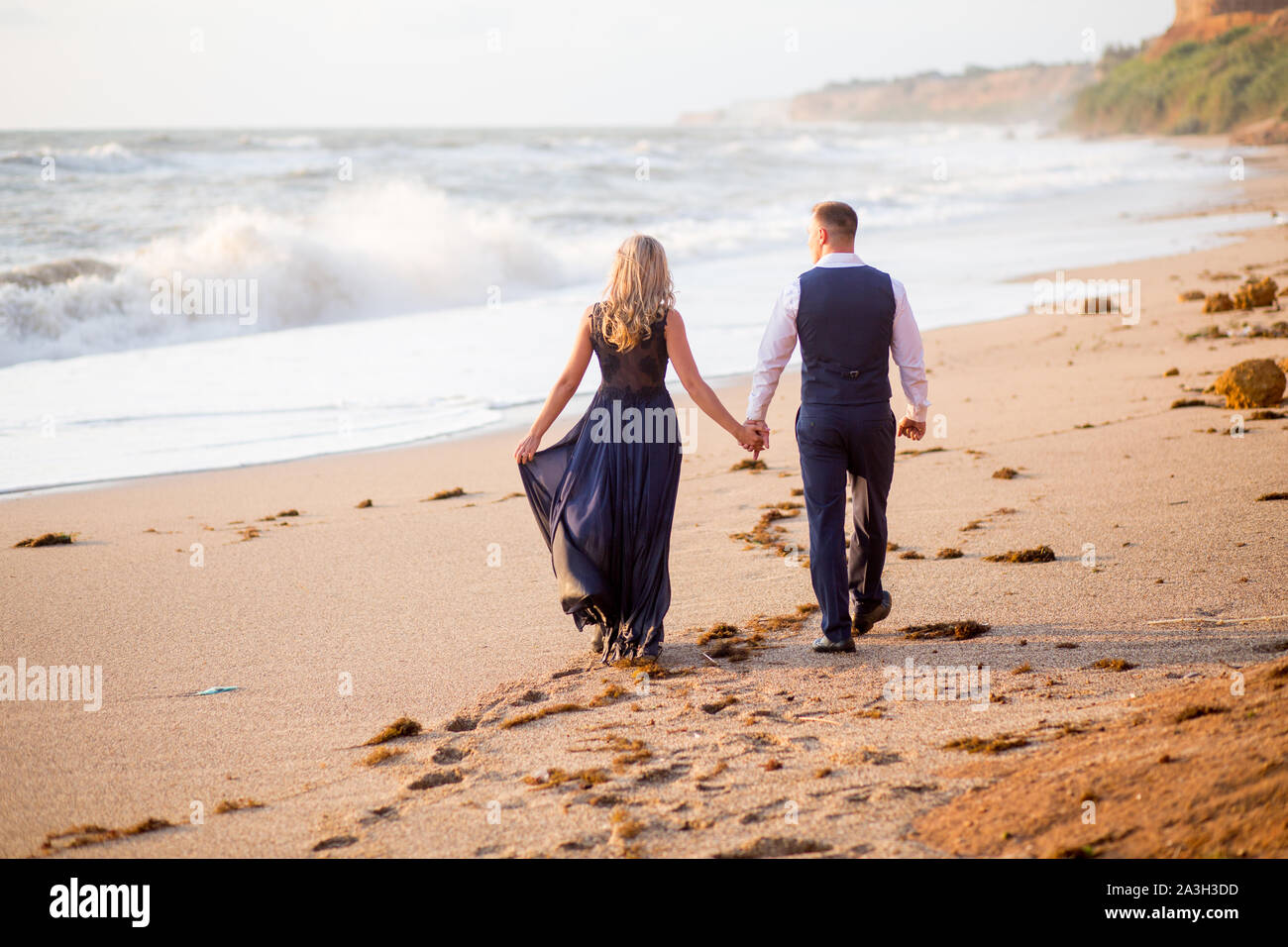 Romantic couple walking at the sunset at the sea coats. Enjoying a beach walk. Stock Photo