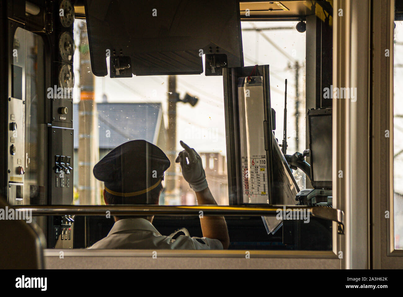 In black and white, a train driver raises his gloved hand in the traditional Japanese "pointing-and-calling" safety ritual (Shisa Kanko) inside the cab of a local train near Hamamatsu, Japan. Stock Photo